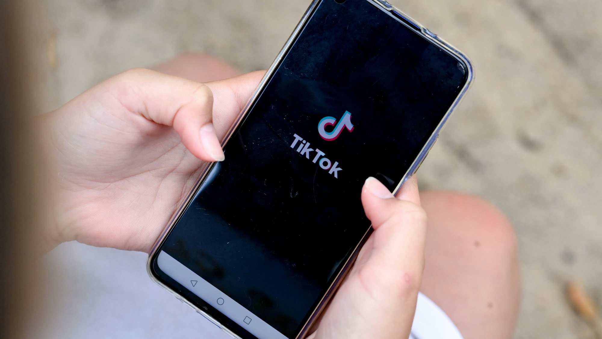 Ein Mädchen hält ein Smartphone in den Händen, auf dem das Logo von TikTok zu sehen ist.