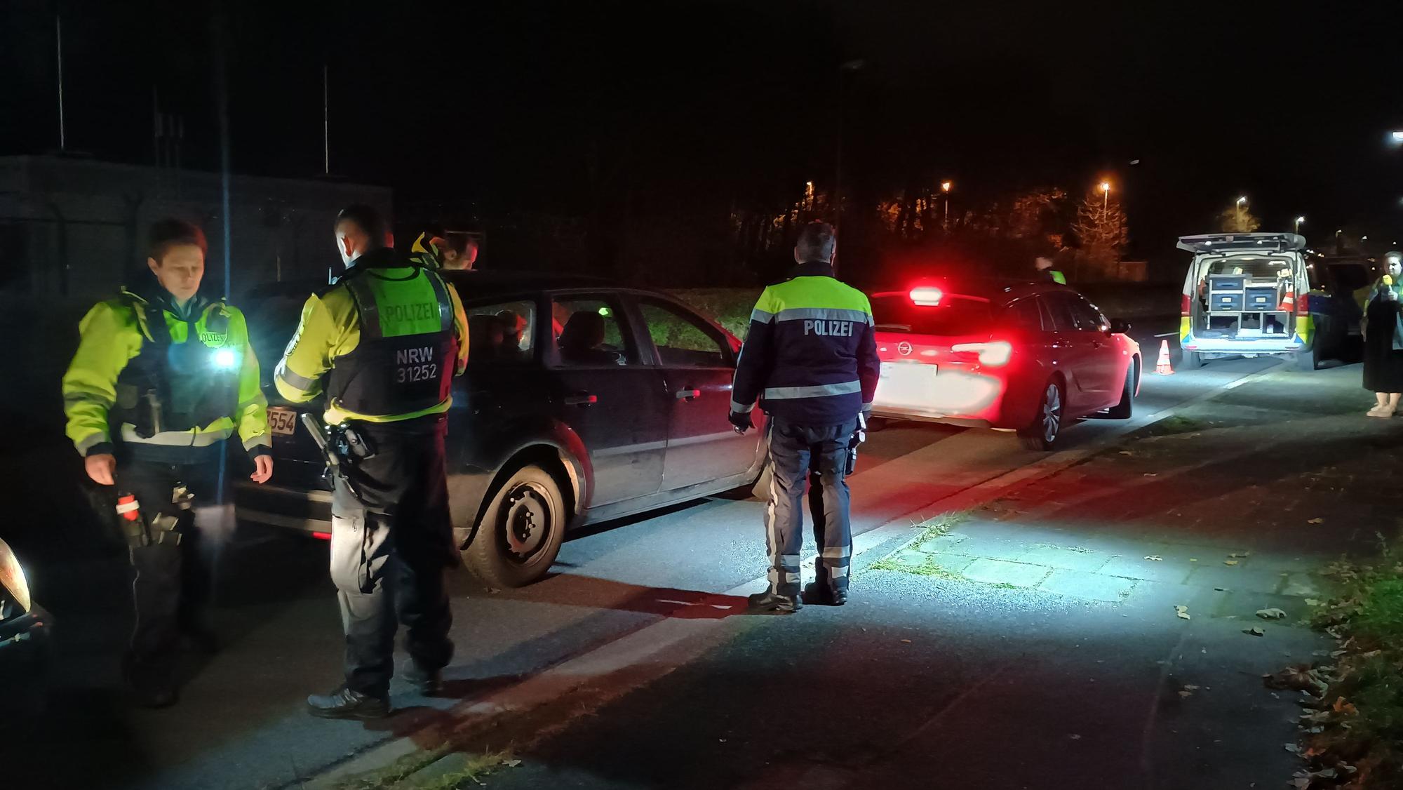 Auf dem Bild sind Polizisten zu sehen, die Autos kontrollieren. Es ist dunkel.