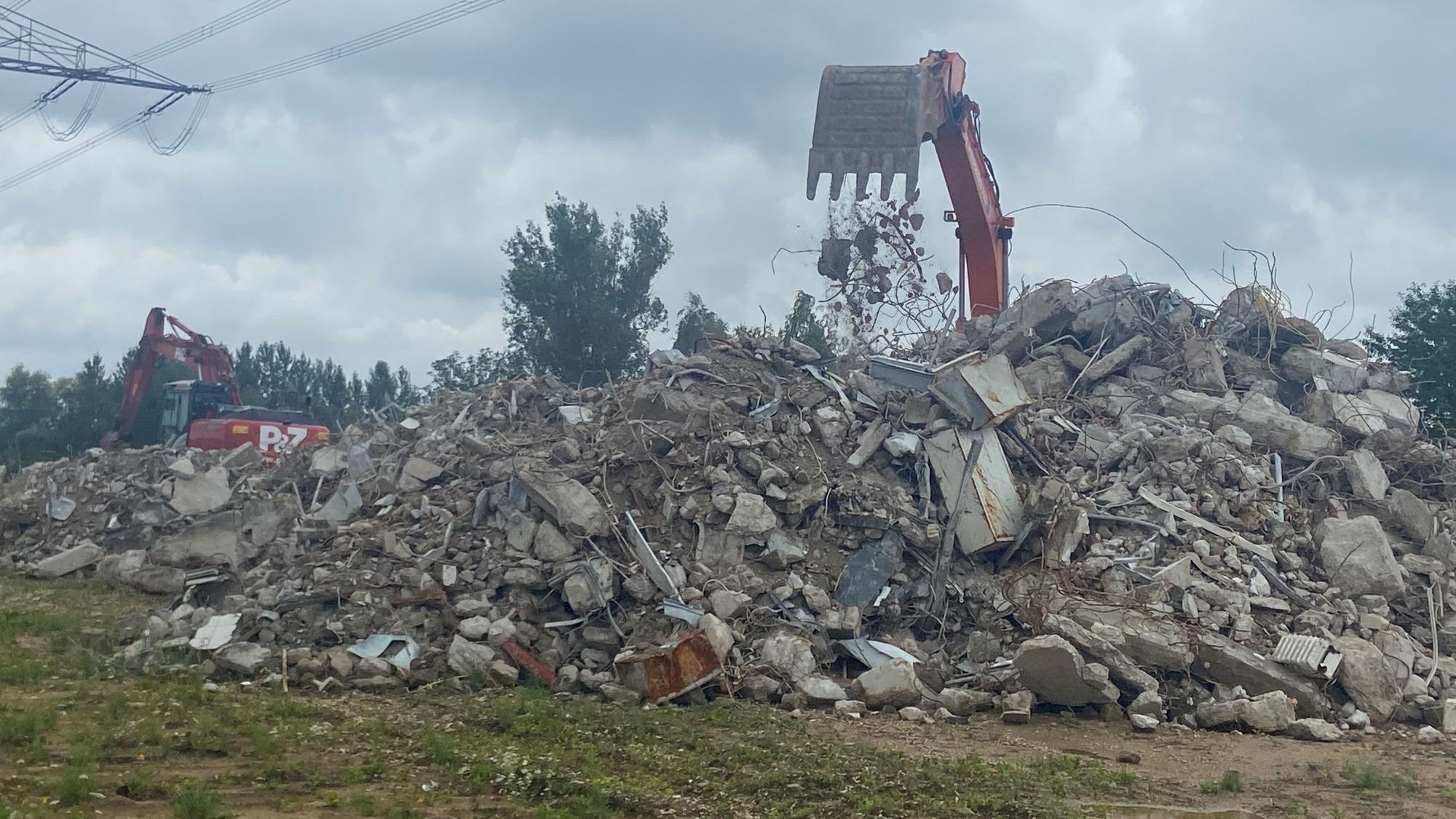 Auf dem Bild ist ein Bagger hinter Schuttbergen zu sehen.