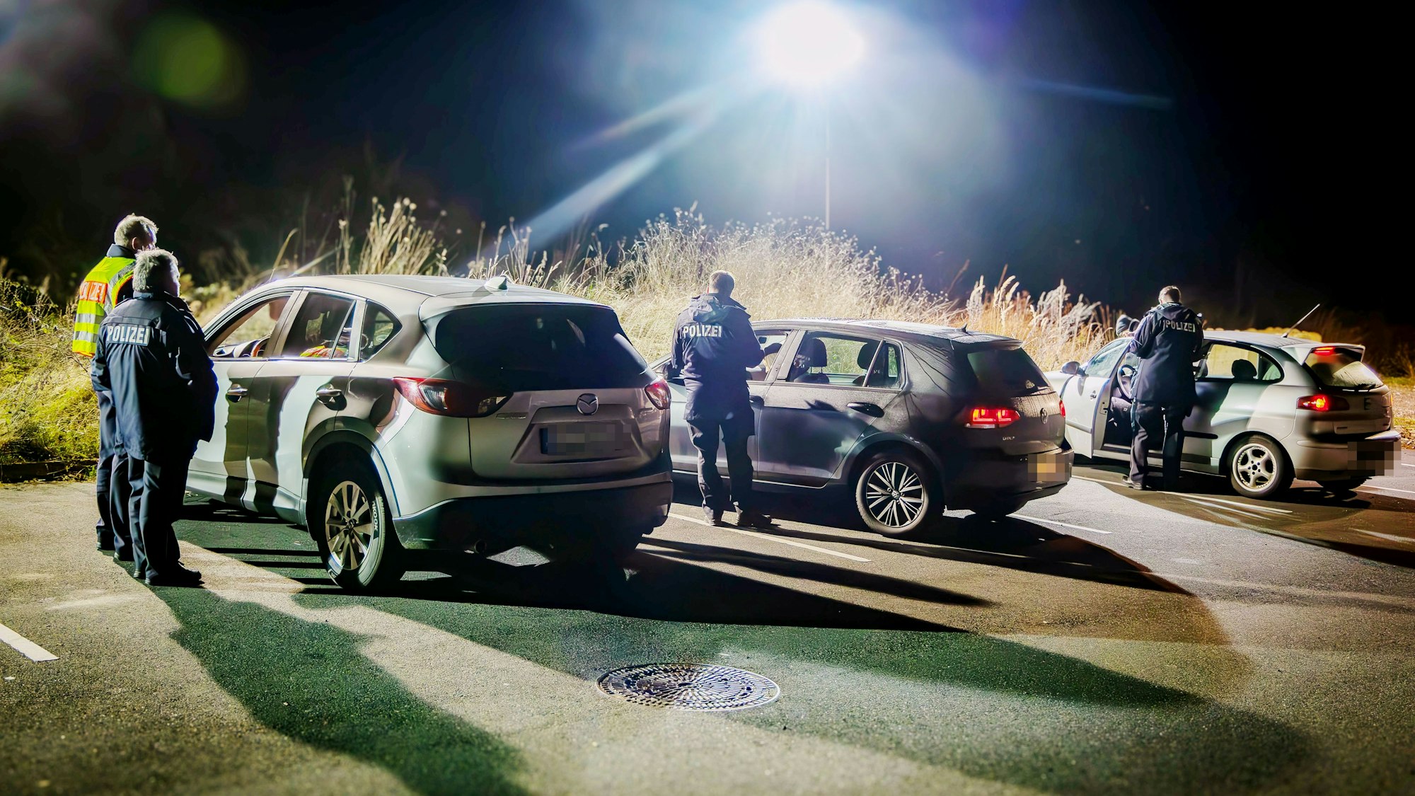 Drei Autos werden im Licht starker Scheinwerfer des Technischen Hilfswerks von Polizeibeamten kontrolliert.