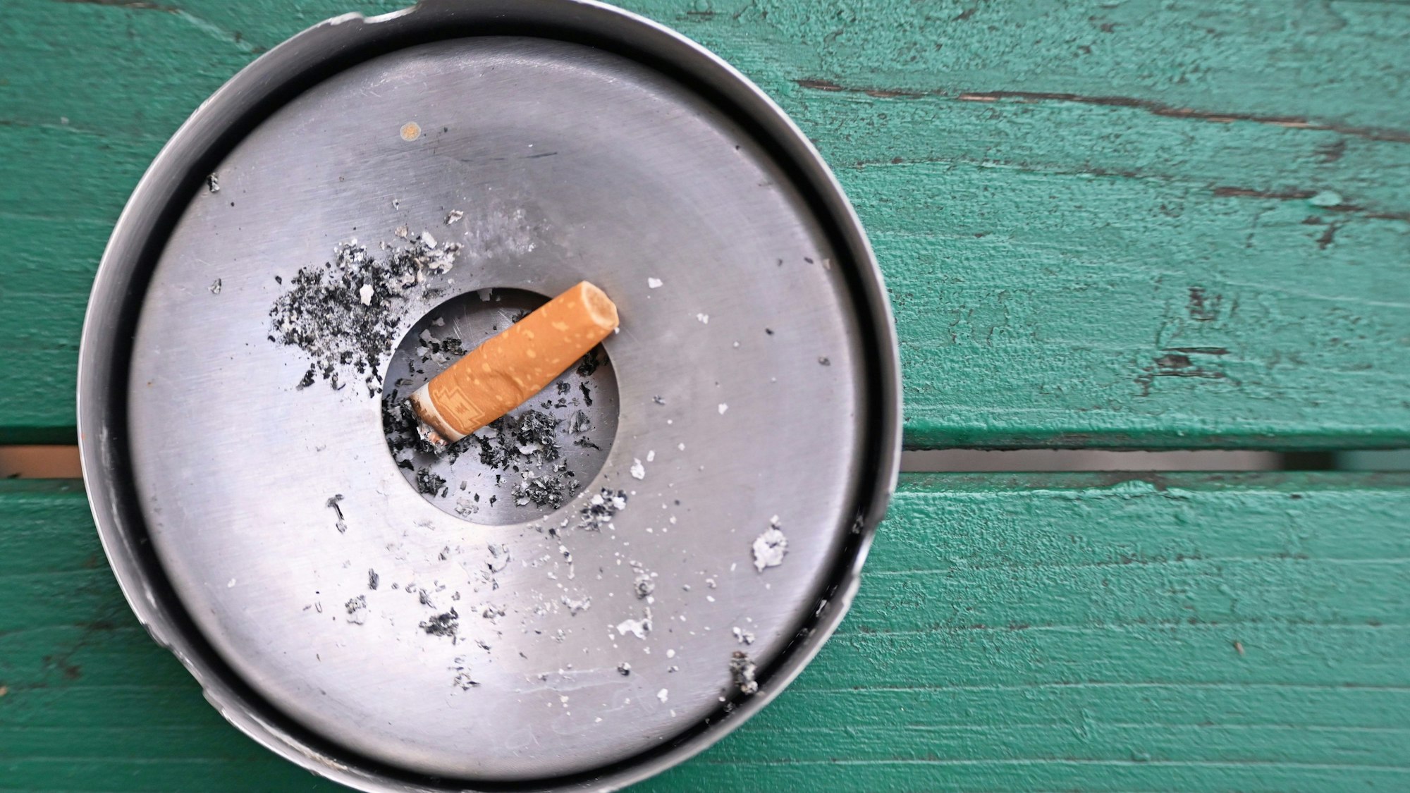 Im Freien liegt eine abgebrannte Zigarette in einem Aschenbecher.