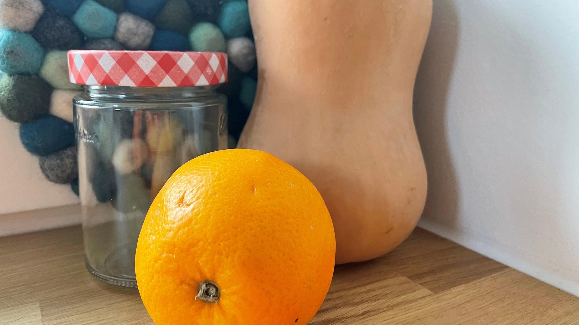 Eine Orange, ein Butternut-Kürbis und ein Marmeladenglas.