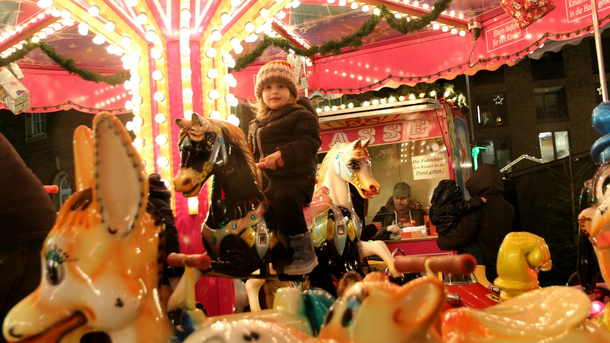 Auf dem Bild ist ein buntes Kinderkarussell zu sehen. Ein junges Mädchen sitzt auf einem der Pferde und fährt im Kreis.