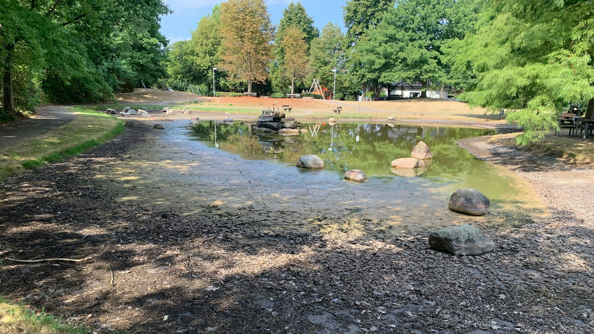 Der Teich neben dem Lauterbach in Birlinghoven trocknet langsam aus. Ein Bild aus dem Jahr 2022. Der Blick auf die Gebäude ist durch Bäume verdeckt.