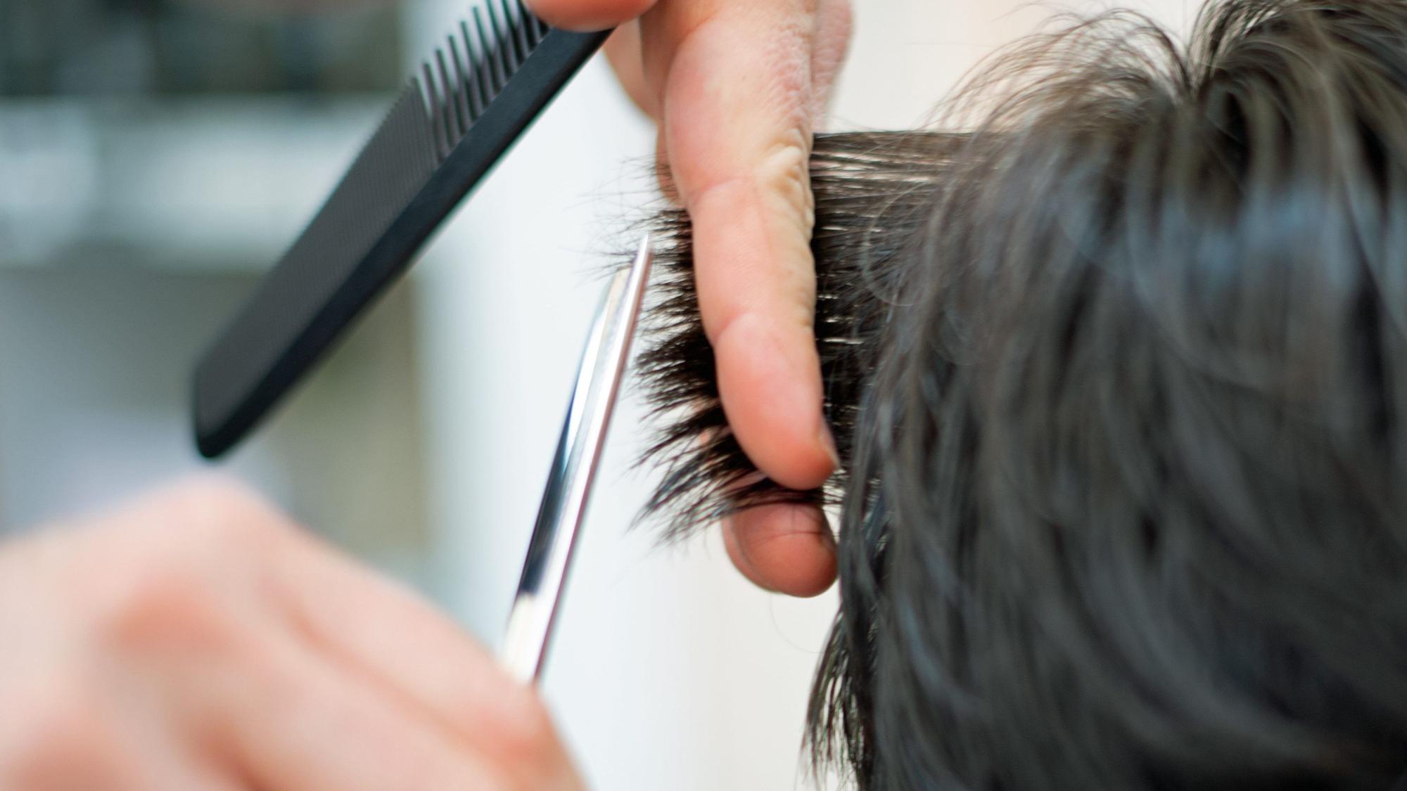 Ein Friseur schneidet in einem Friseursalon einer Kundin mit einer Schere die Haare.
