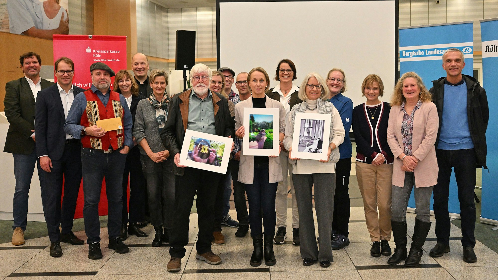 Preisträger des Fotowettbewerbs „Foto des Jahres 2024“ stehen mit Vertretern von Bergischer Landeszeitung, Kölner Stadt-Anzeiger und Wettbewerbspartner Kreissparkasse Köln am Mittwochabend (27.11.) bei der Preisverleihung in  der Kassenhalle der Regionalfiliale der Kreissparkasse Köln Bergisch Gladbach.
