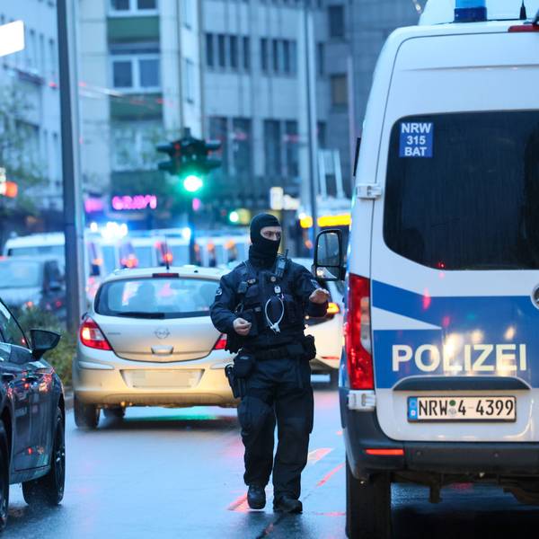 Polizeibus und ein vermummter Beamter sind im Straßenverkehr zu sehen.