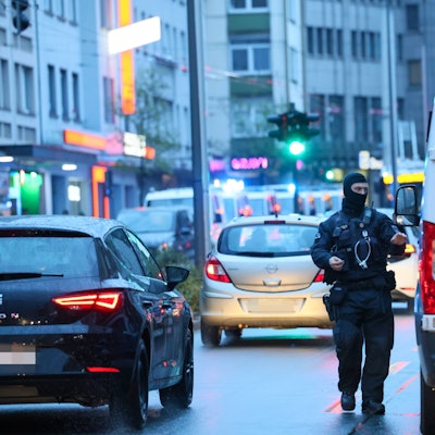 Polizeibus und ein vermummter Beamter sind im Straßenverkehr zu sehen.
