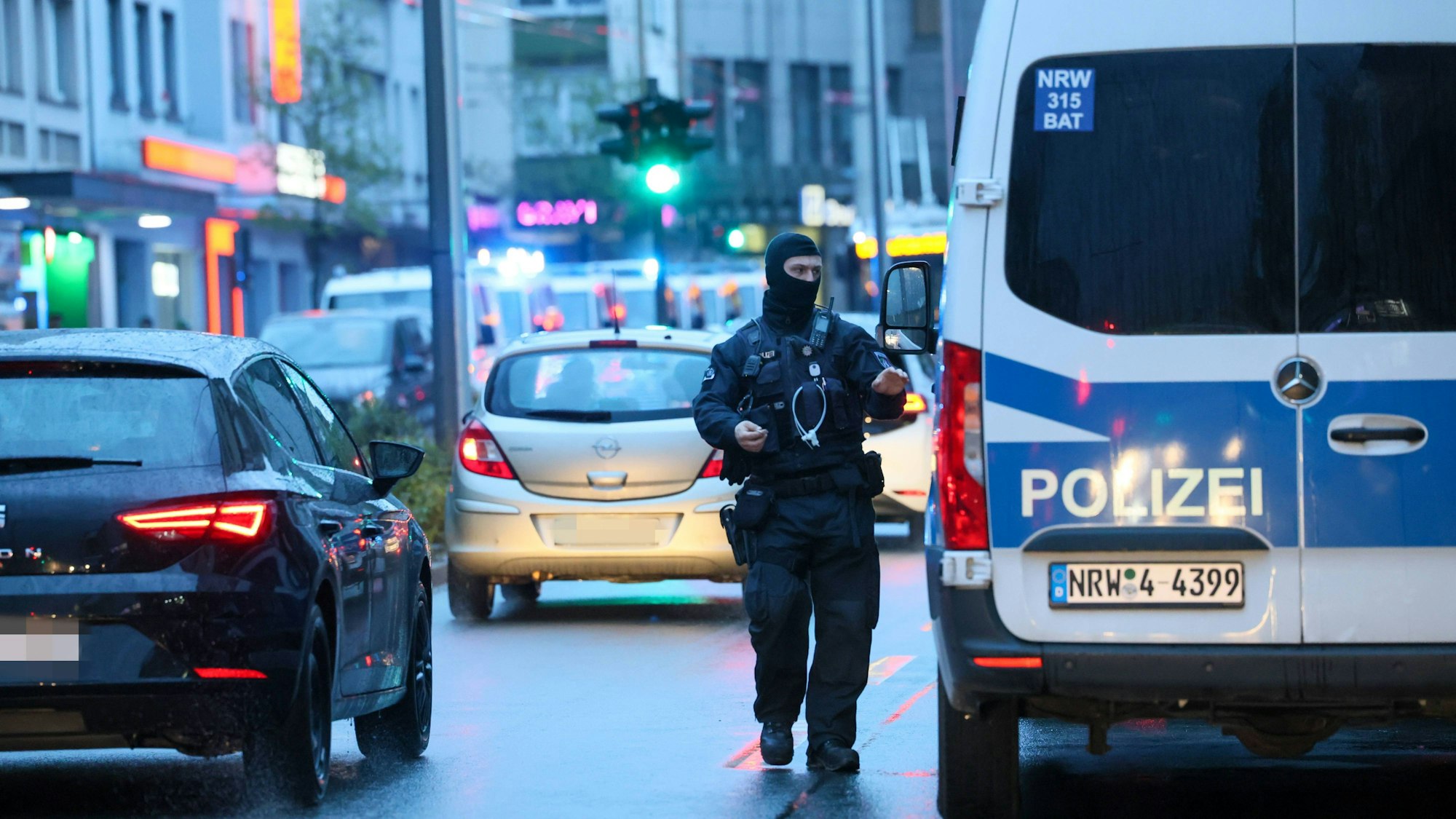 Polizeibus und ein vermummter Beamter sind im Straßenverkehr zu sehen.