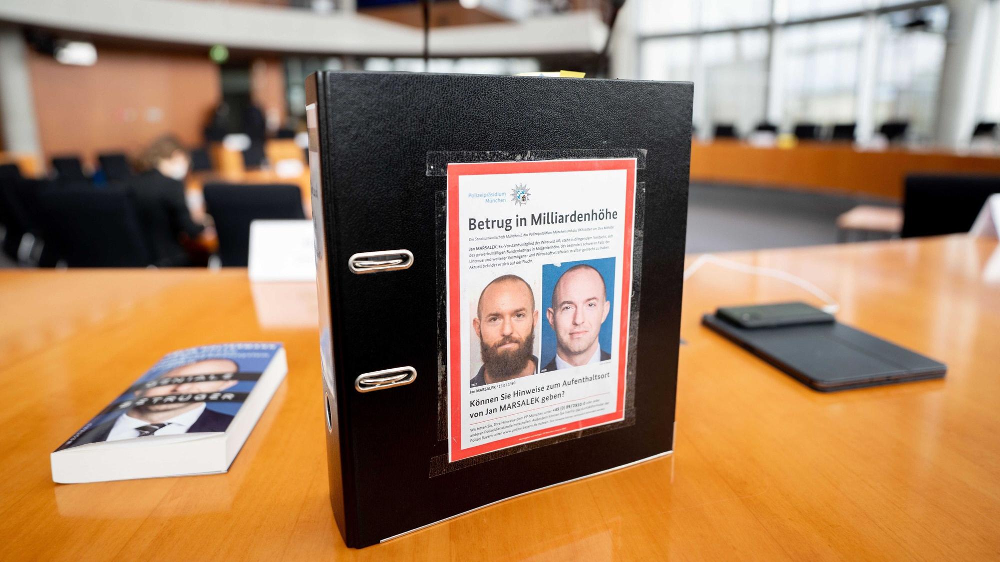 ARCHIV - 15.04.2021, Berlin: Der Aktenordner des ehemaligen Bundestagsabgeordneten de Masi (Die Linke) mit Fahndungsfotos des früheren Wirecard-Finanzvorstands Jan Marsalek ist im Sitzungssaal zum Bilanzskandal Wirecard im Paul-Löbe-Haus zu sehen.