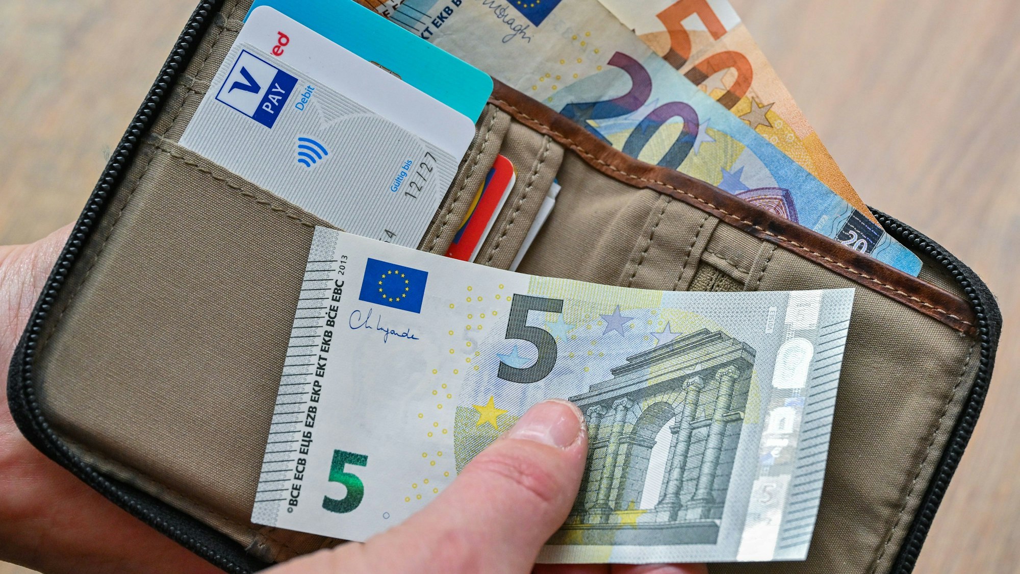 Eine Frau hält in ihrer Hand eine Brieftasche mit Geld und Bankkarten.