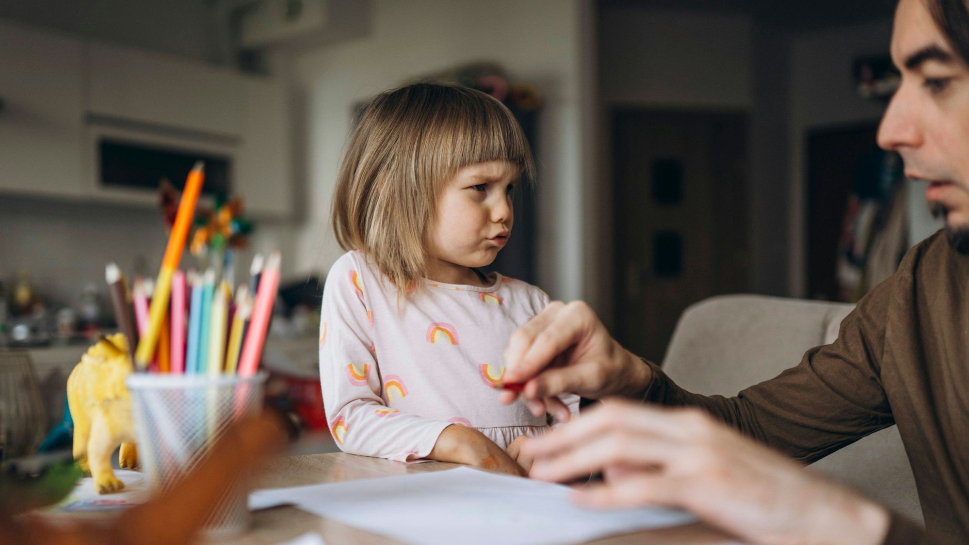 Ein Vater bringt seiner traurigen Tochter zu Hause das Zeichnen bei. Das Foto steht symbolisch für die Alltagsprobleme mancher Alleinerziehender.