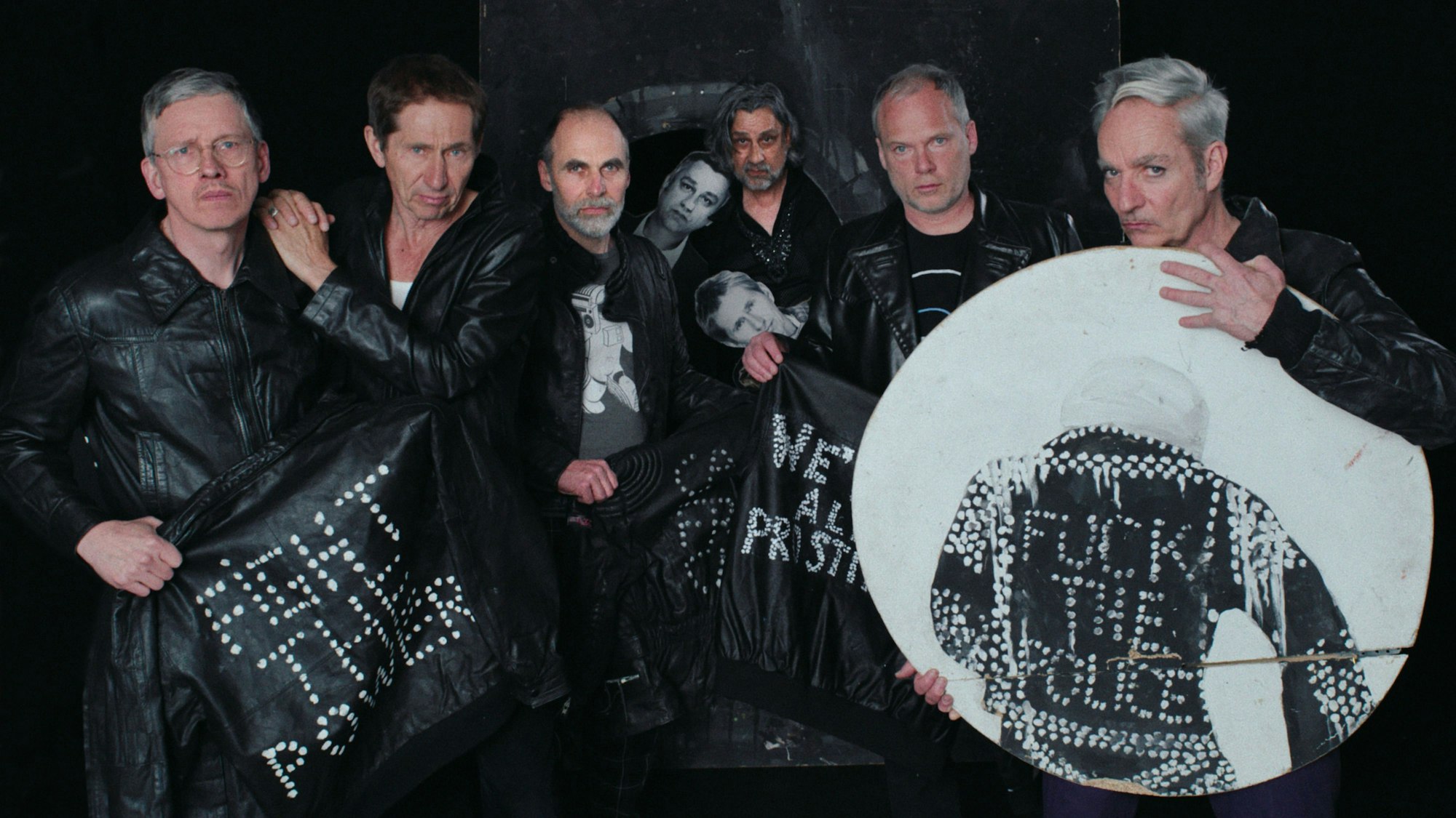 Die Goldenen Zitronen tragen schwarze Lederjacken und halten weitere Lederjacken und ein Bild mit Punk-Slogans - "Fight the Power", "Fuck the Police" - hoch.