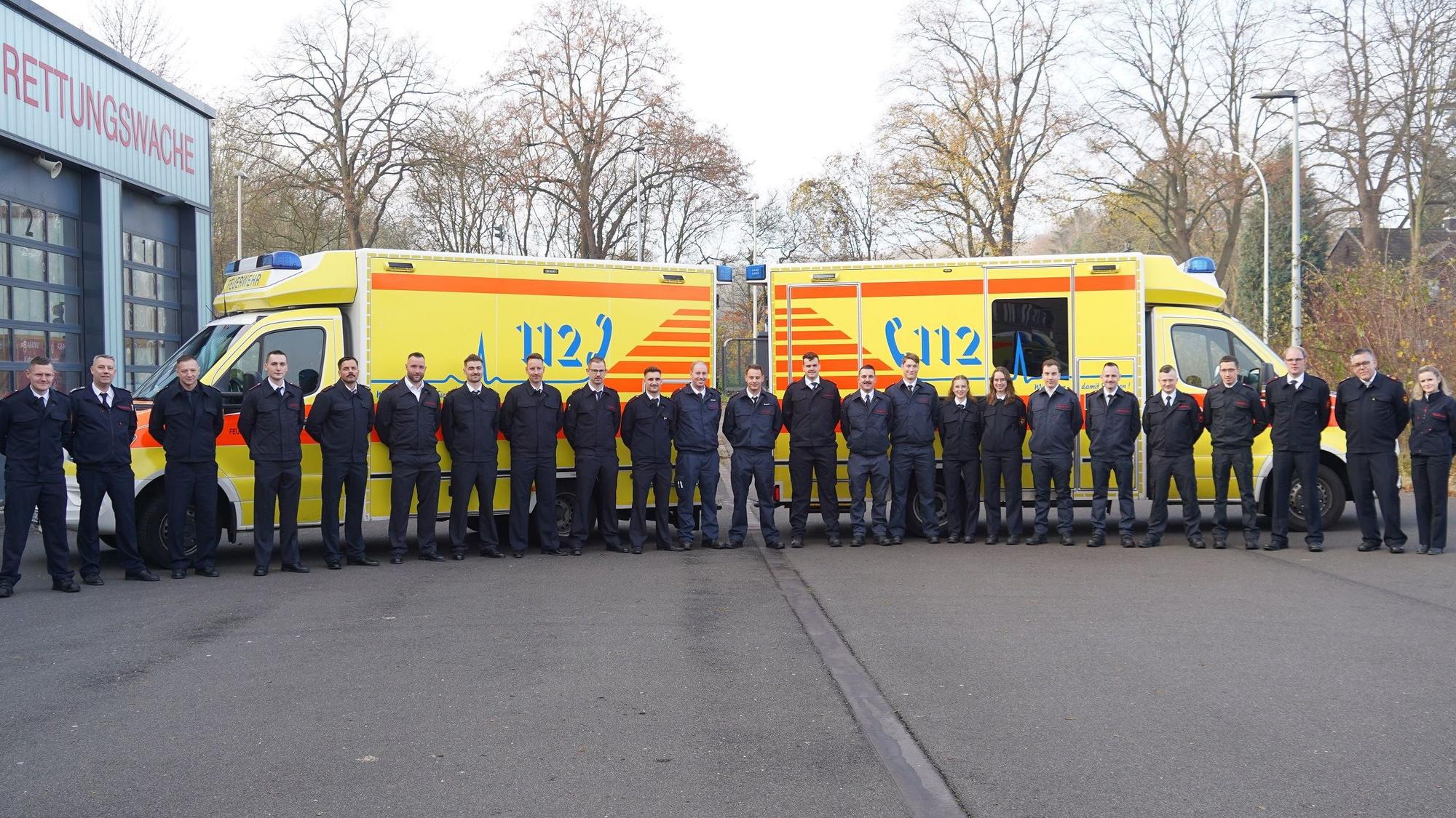 Auf dem Bild sind zwei Krankenwagen und eine Gruppe von Menschen in Uniform zu sehen.