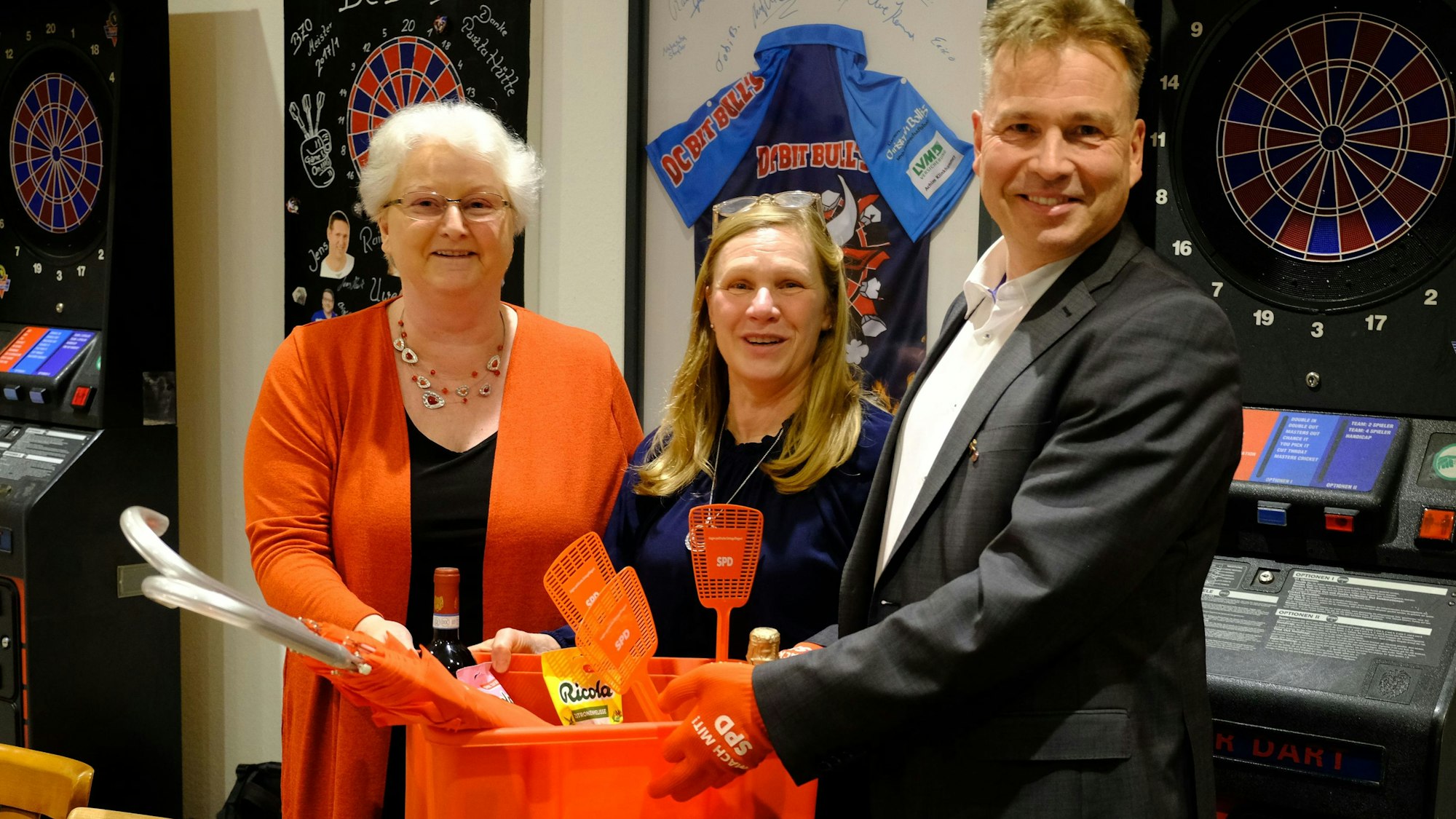 SPD-Ortsvereinsvorsitzende Ute Wagener (l.) überreicht Dr. Peter Schweikert-Wehner eine rote Plastikkiste. In der Mitte die Ehefrau des Kandidaten, Dr. Kirstin Wehner.