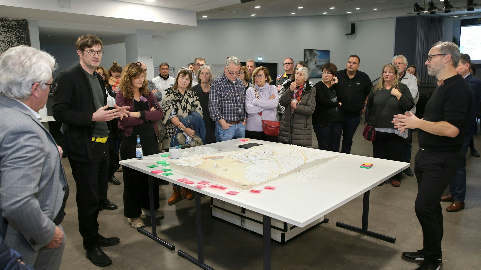 Frauen und Männer stehen um einen Tisch mit einem Modell und diskutieren.