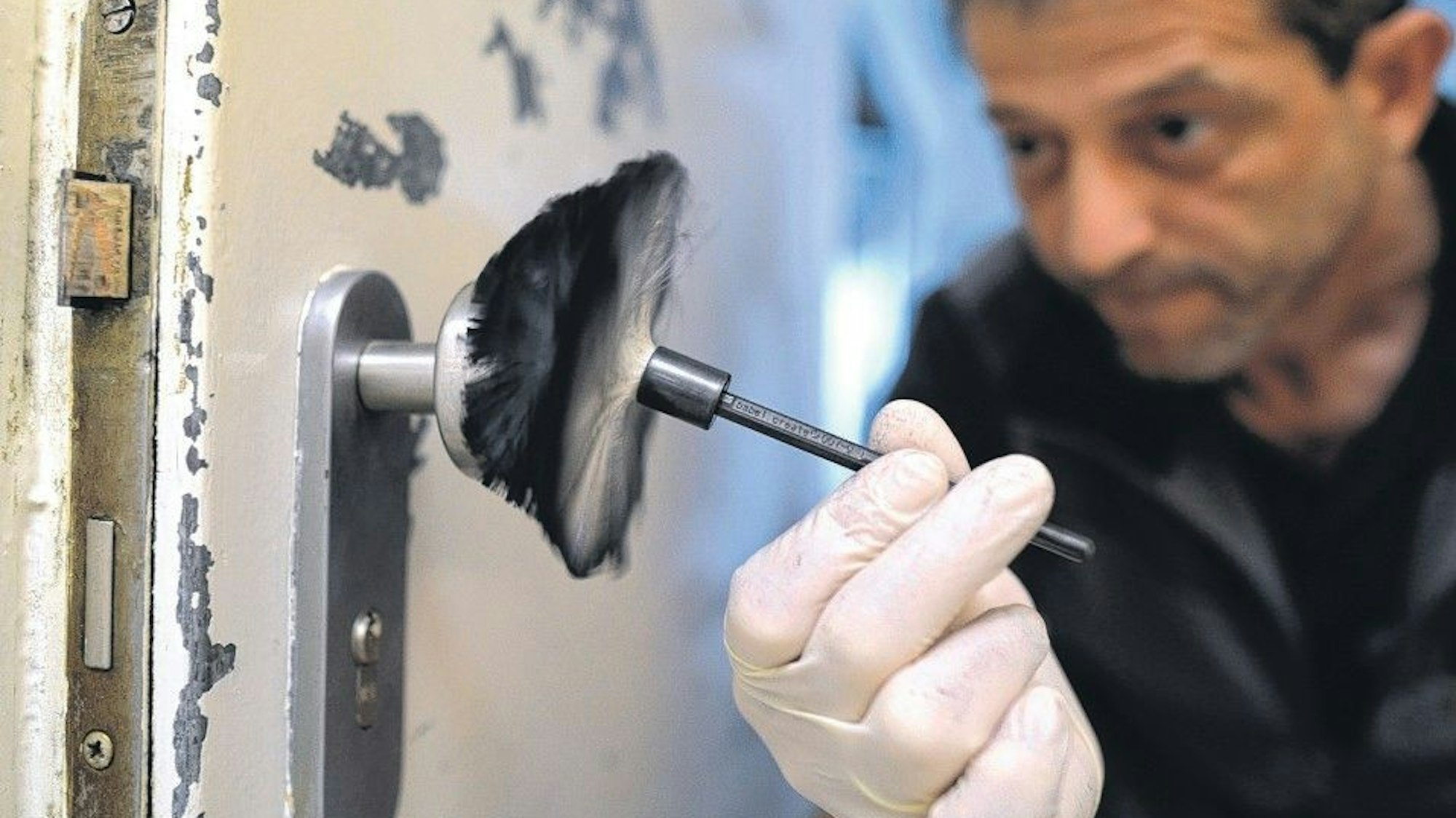 Ein kriminaltechnischer Angestellter der Polizei sichert Spuren an einer Eingangstür.