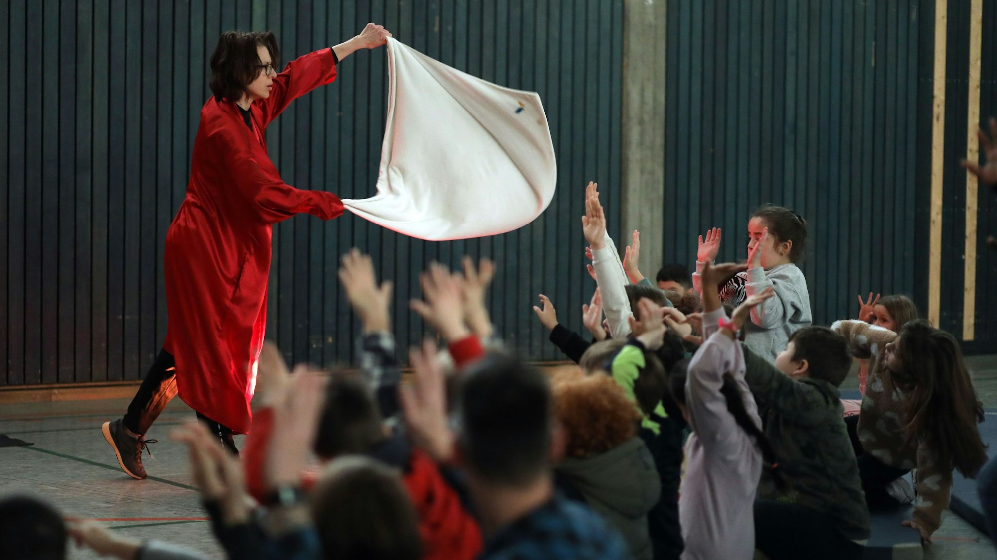 Eine Tänzerin, die als Saunameisterin verkleidet ist, wedelt den Grundschulkindern mit einem Tuch Luft zu.
