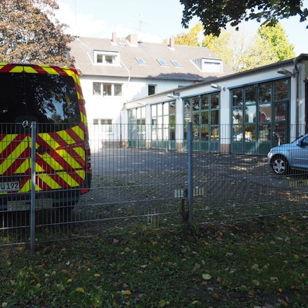Links vorne ein Einsatzfahrzeug vor einem Feuerwehrgerätehaus.