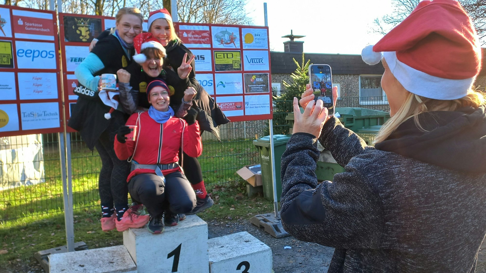 Beim Glühweinlauf 2024 des VfR Marienhagen fotografiert eine Frau vier andere Frauen, die auf einem Siegertreppchen stehen.
