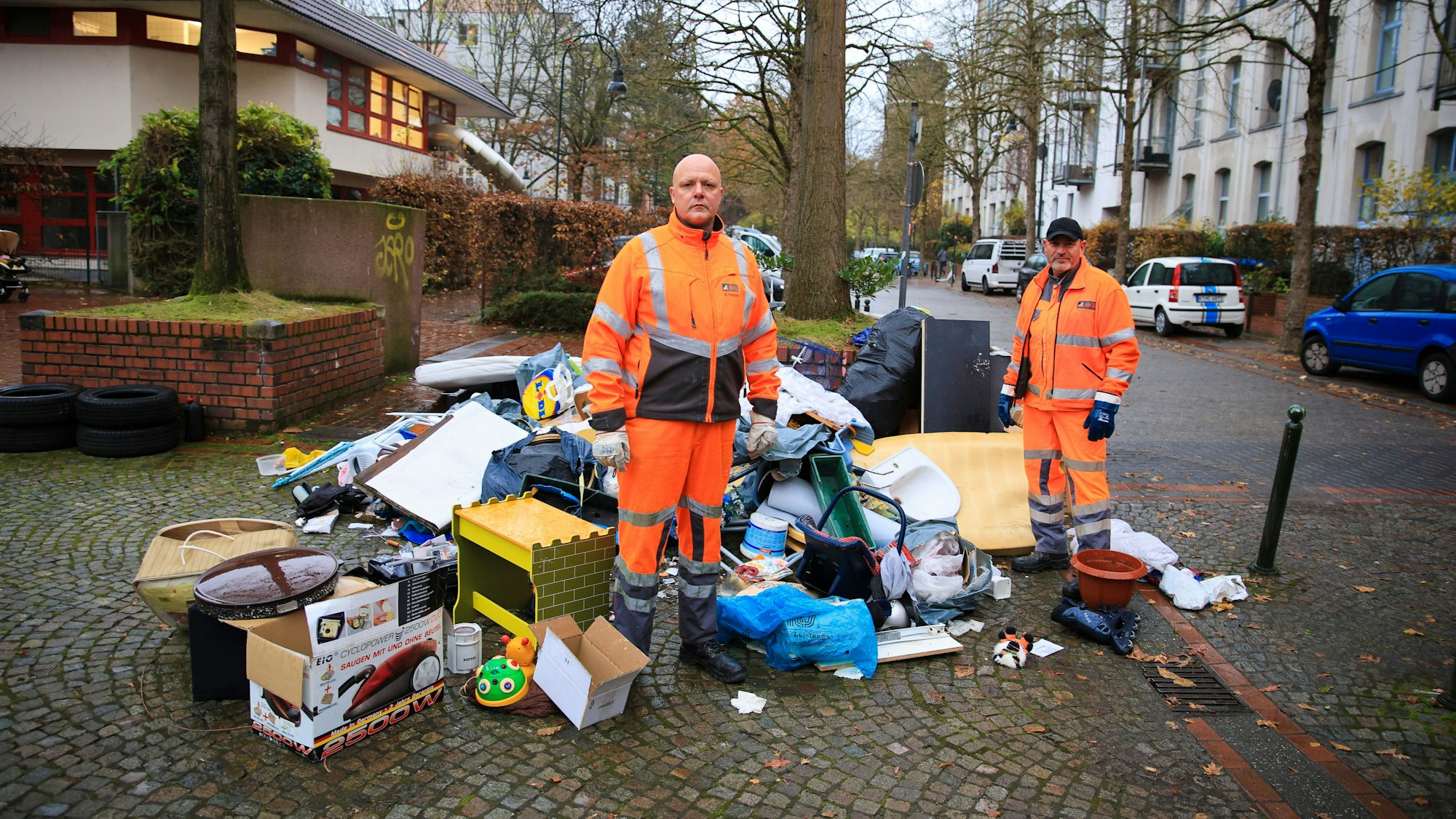Illegal entsorgter Müll mitten in der Kölner Südstadt. Die AWB-Männer Georg Happe (l.) und Olaf Jablonski laden pro Tag viele solcher Haufen ein.