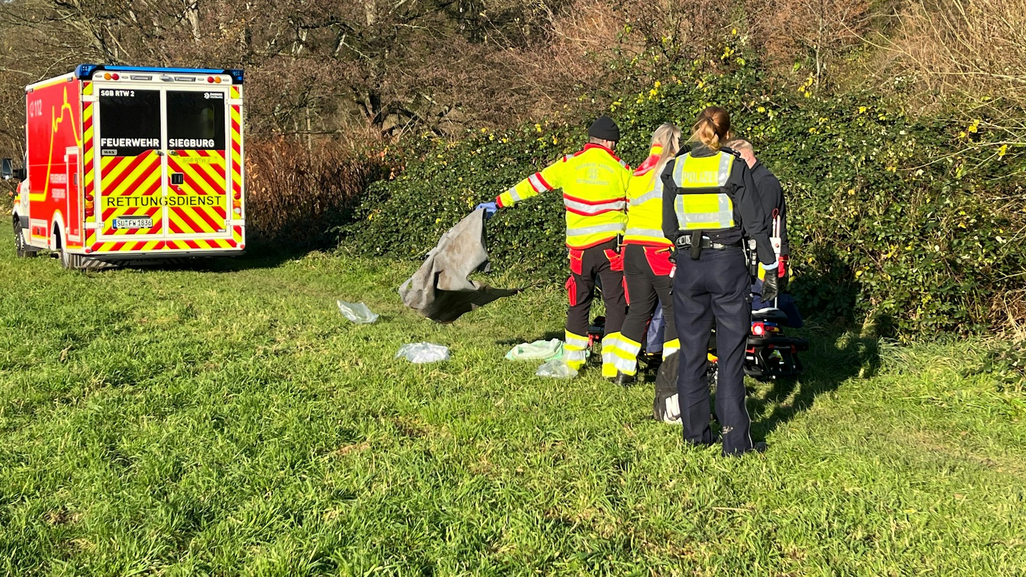 Polizisten und Mitarbeiter des Rettungsdienstes stehen vor einer Trage mit dem unterkühlten Mann.