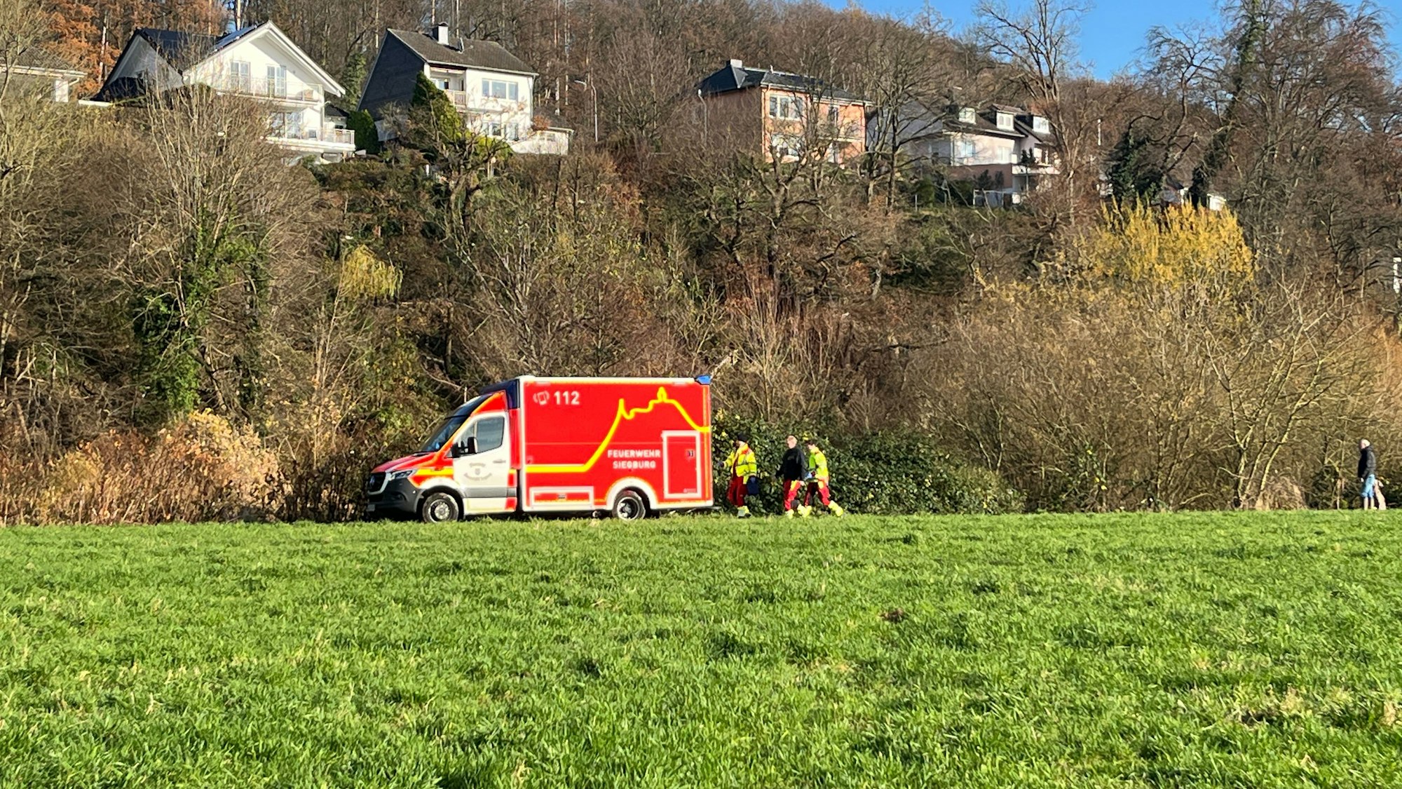 Ein Rettungswagen steht am Ufer der Sieg, die Besatzung steht dahinter.
