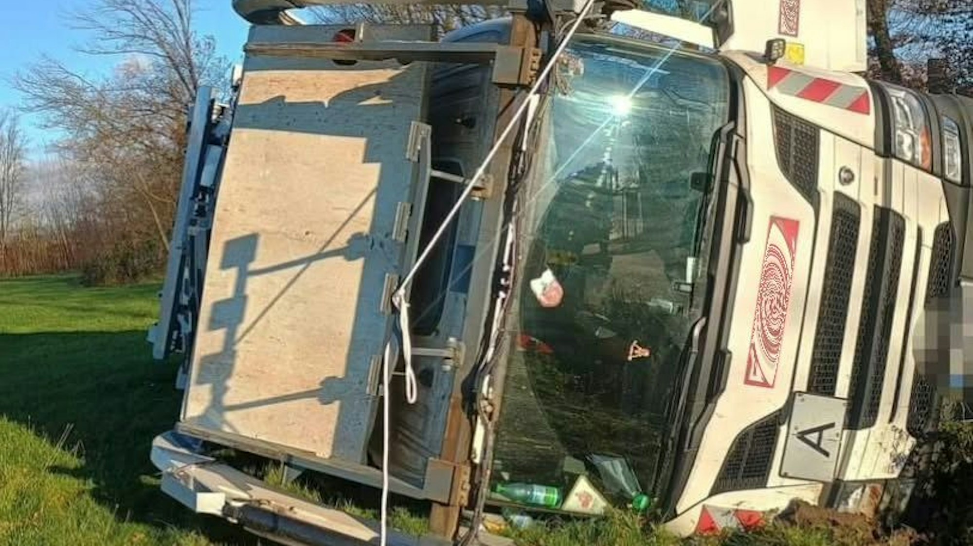 Ein Müllfahrzeug liegt auf der Seite in einer Wiese.