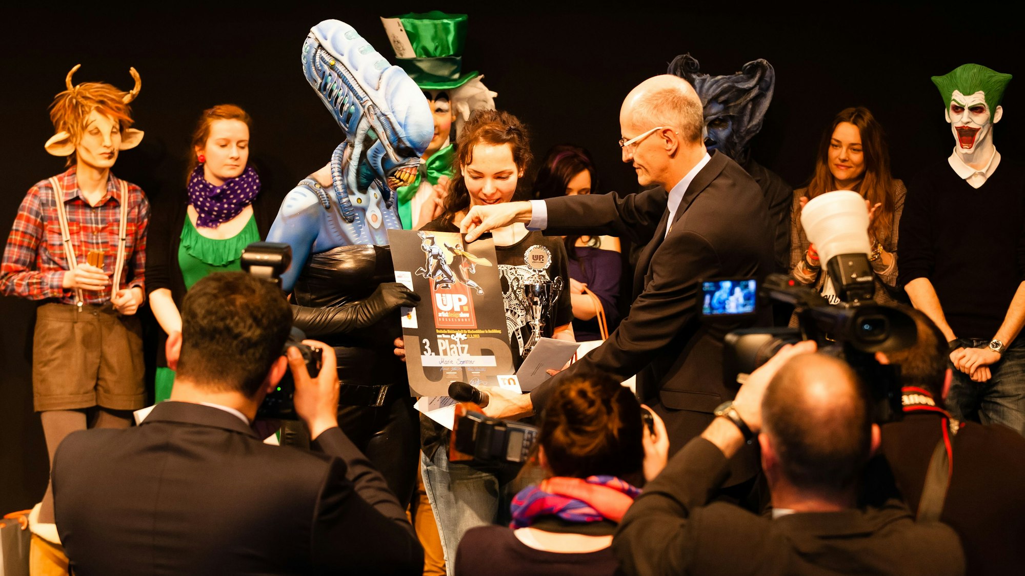 Menschen mit aufwendig gestalteten Masken bei einer Preisverleihung.