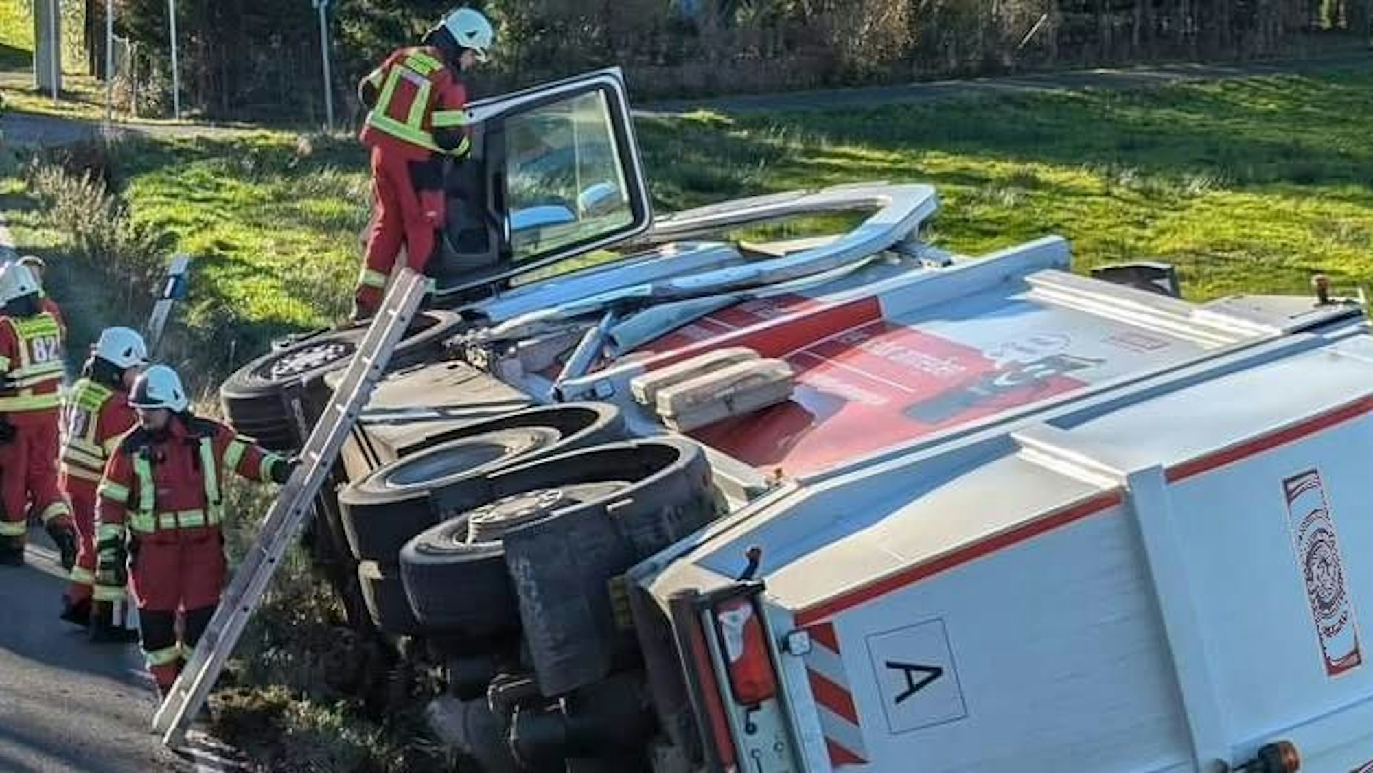 Ein Müllwagen liegt auf der Seite, ein Feuerwehrmann ist über eine Leiter zum Fahrerhaus hinaufgeklettert.