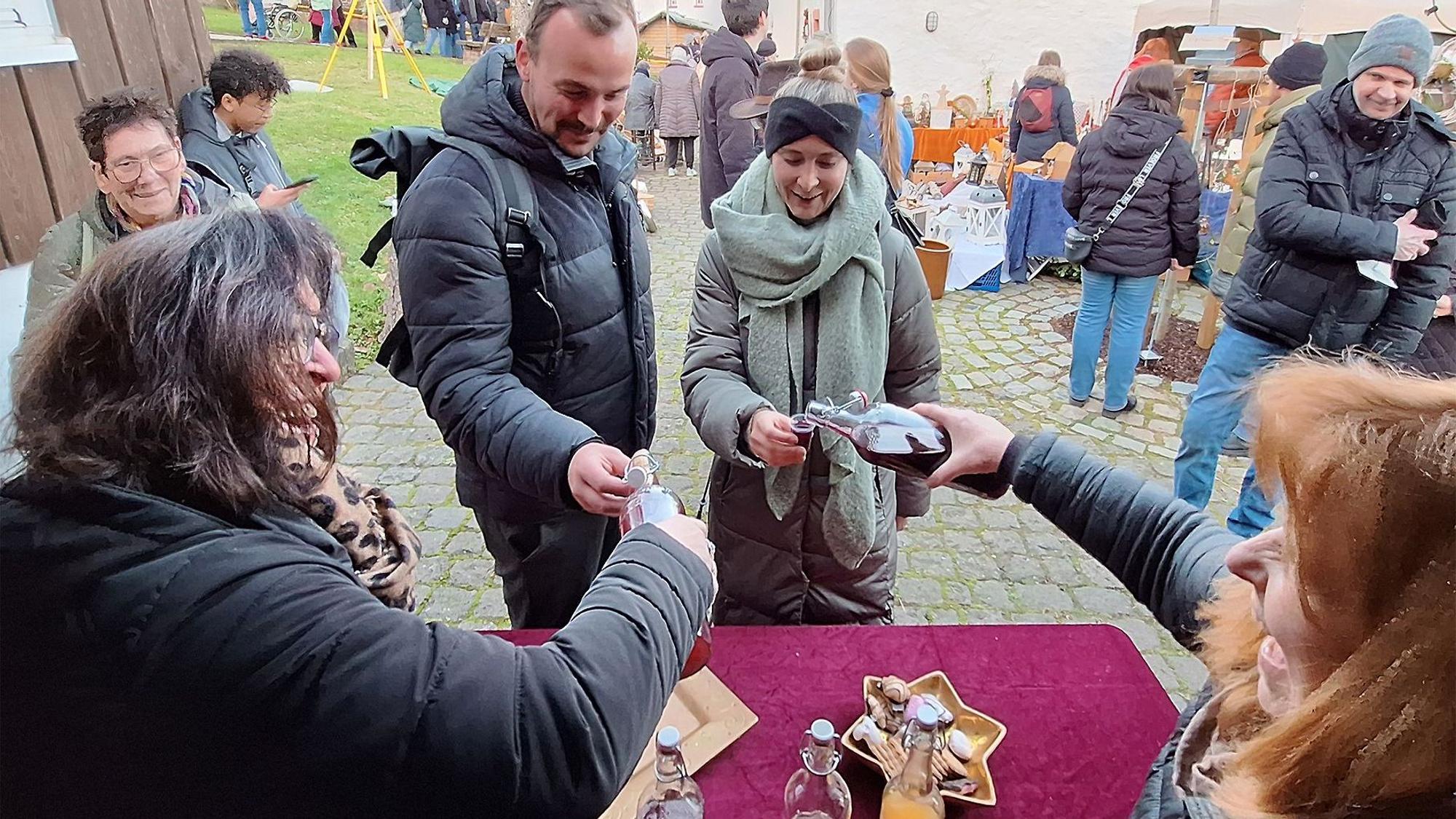Das Bild zeigt Carmen und Elke Huppertz, die Gästen vor ihrem Stand einen Likör einschenken.