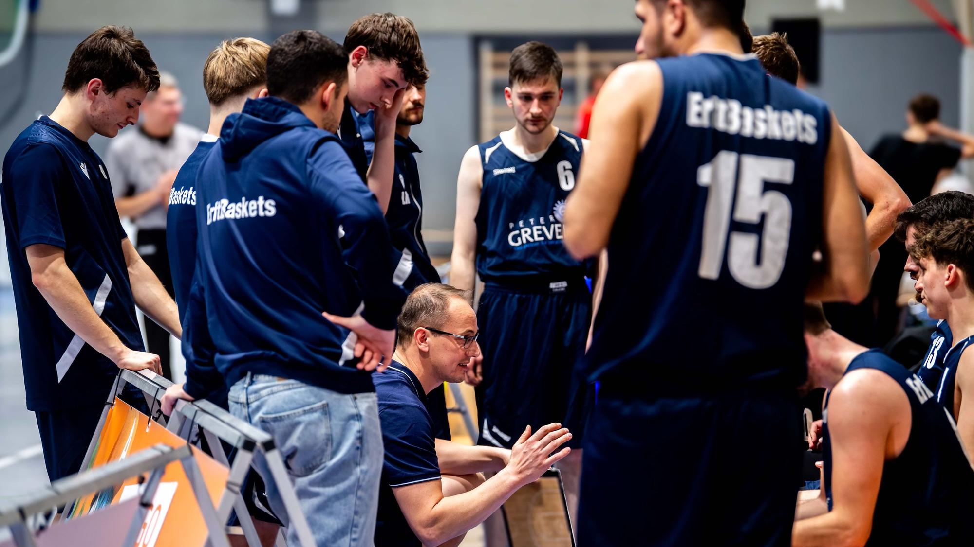 Der bisherige Trainer Florian Hammes gibt seiner Mannschaft Anweisungen und hockt dabei inmitten seiner Spieler.