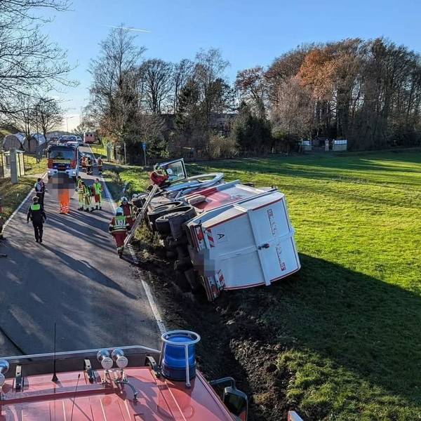 Ein Müllwagen liegt auf der Seite in einer Wiese, Feuerwehrleute steigen auf einer Leiter zur Fahrertür hinauf.