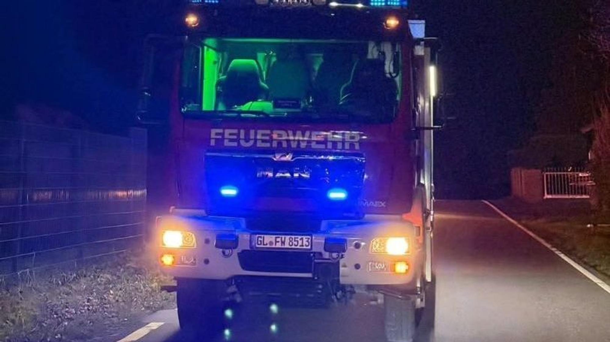 Ein Feuerwehrfahrzeug mit ausgefahrenem Lichtmast steht auf der dunklen landstra0e 84 bei Overath-Hufe.