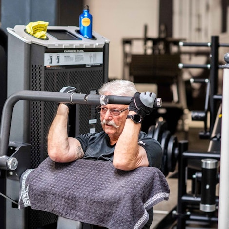 Das Bild zeigt Peter aus Wünschheim auf einem Sportgerät, mit dem man seinen Bizeps trainiert.