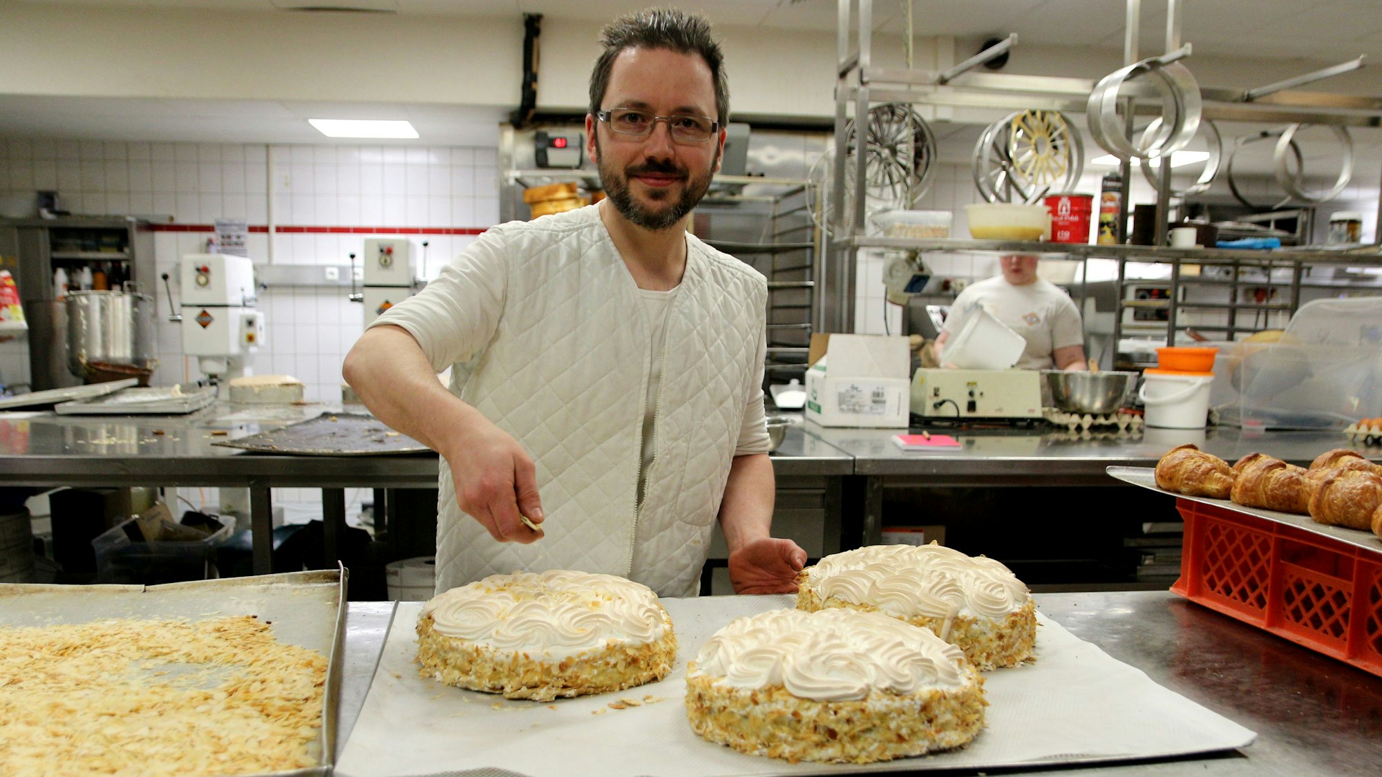 Ein Konditor dekoriert in seiner Backstube drei Torten.