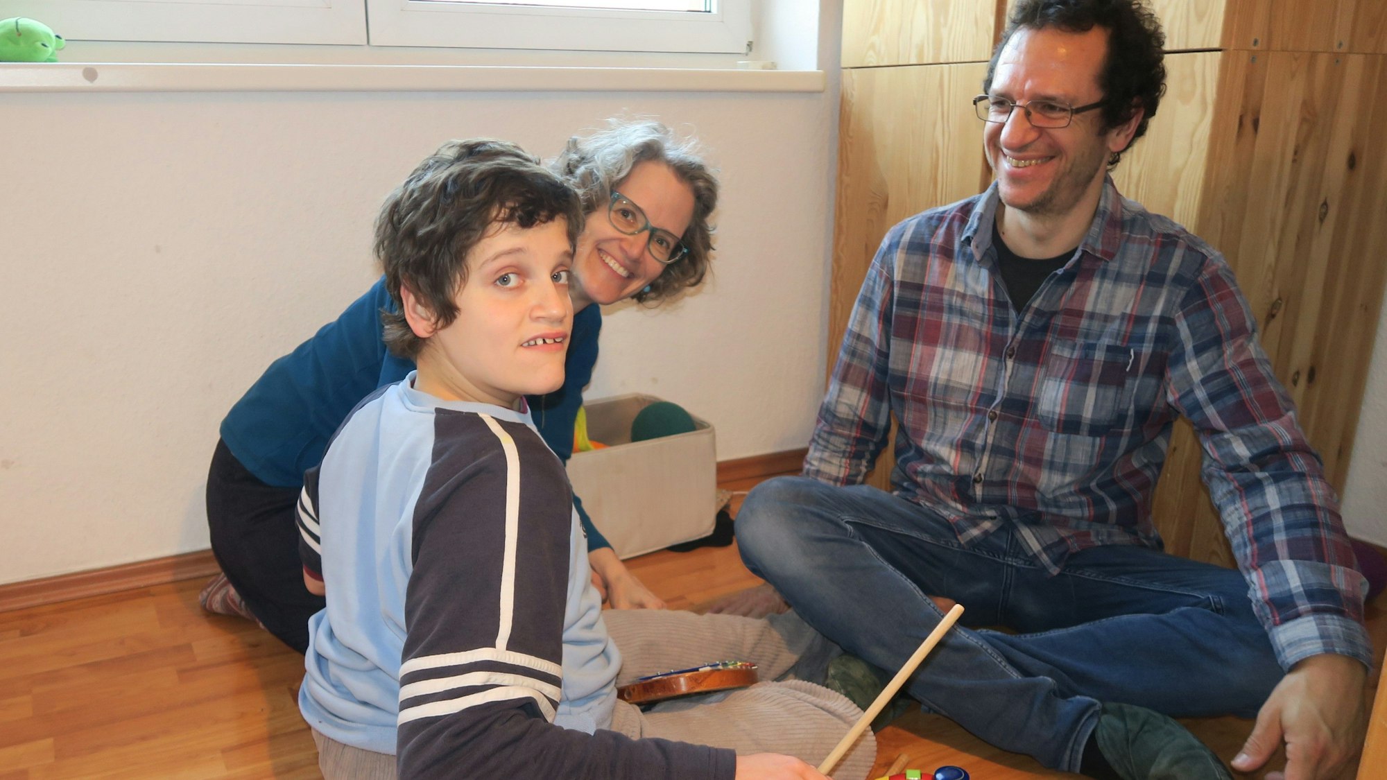 Ein Elternpaar sitzt mit einem großen Jungen auf dem Boden.