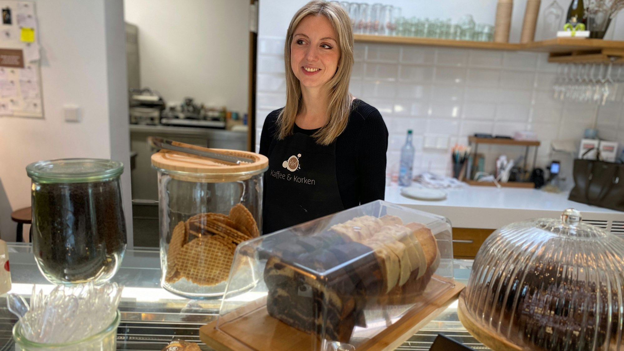 Janine Munder steht hinter der Theke, darauf stehen durchsichtige Behältnisse mit Kuchen und Keksen.