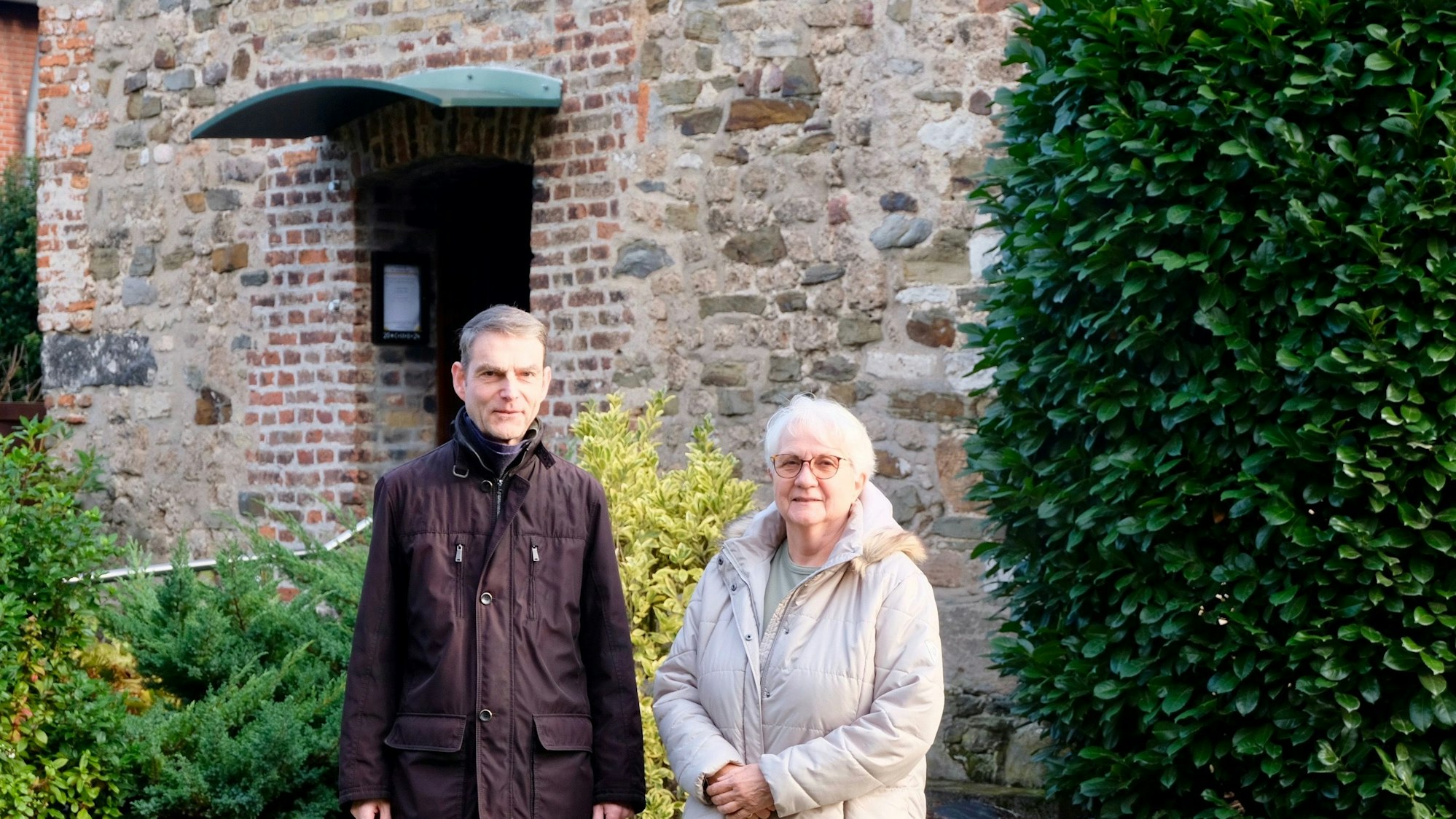 Ein Mann und eine Frau stehen vor einer alt aussehenden Fassade einer Kapelle.