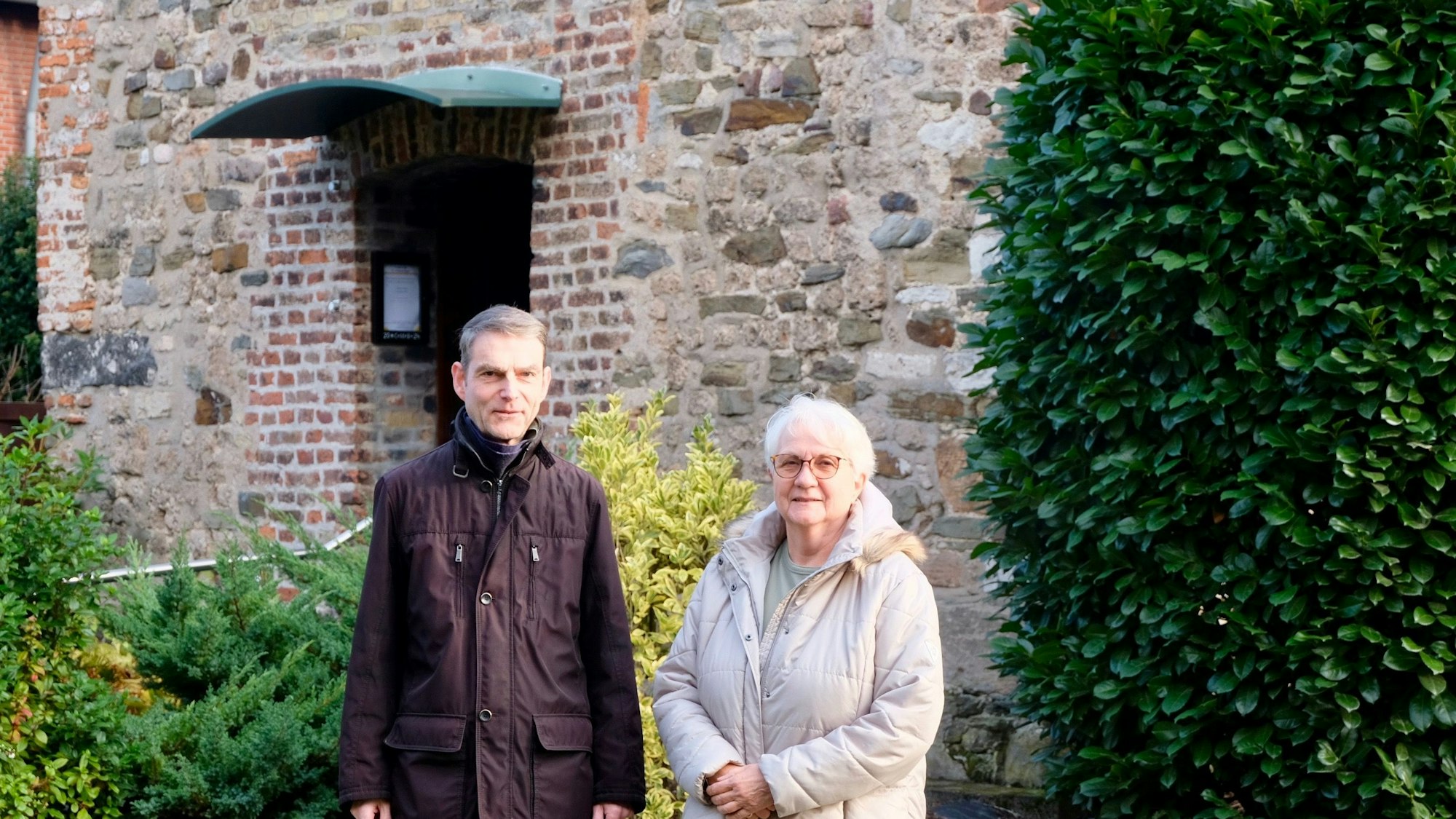 Ein Mann und eine Frau stehen vor einer alt aussehenden Fassade einer Kapelle.