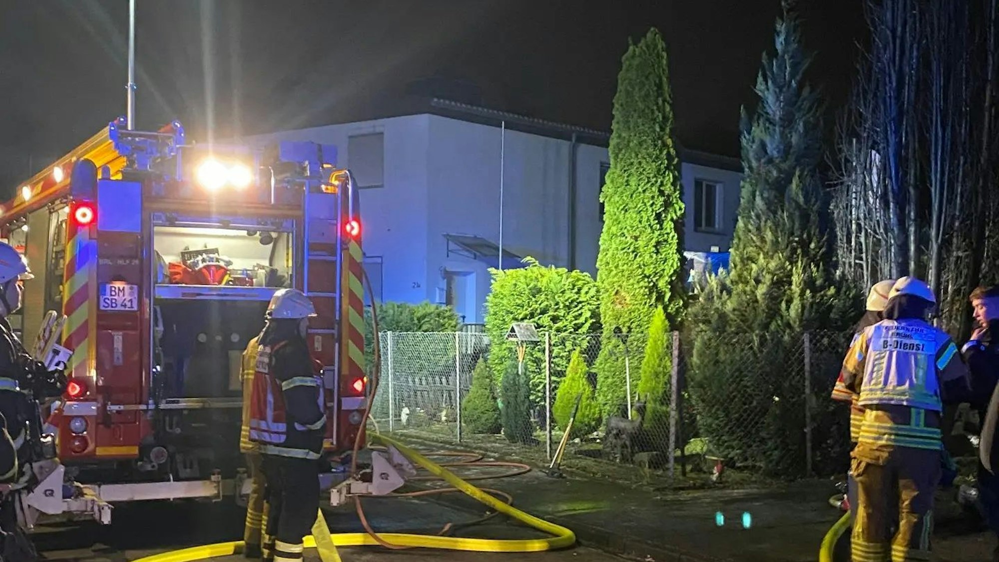 Feuerwehrfahrzeug, ein gelber Schlauch und Einsatzkräfte. Rechts eine verkohlte Konifere.