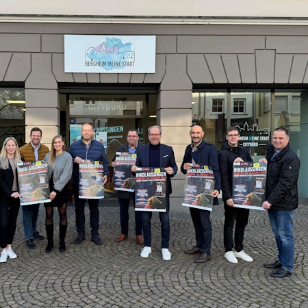 Zu sehen sind verschiedene Akteure aus Stadt und Kultur, die Plakate für das Nikolaussingen hochhalten.