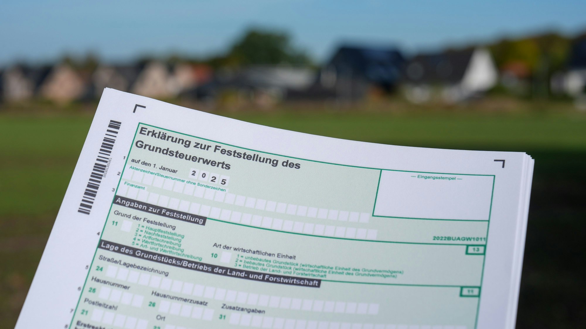 Ein Erklärung zur Feststellung des Grundsteuerwerts für das Jahr 2025 wird vor einer Wohnsiedlung hochgehalten.