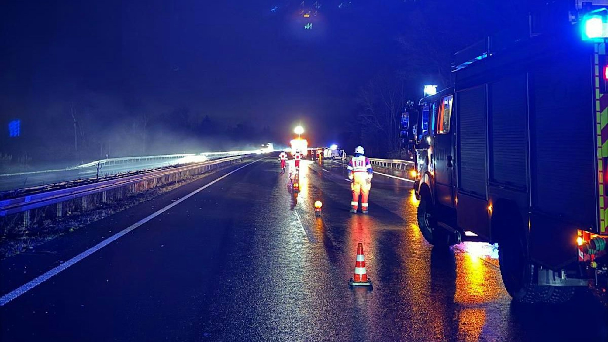 Feuerwehrleute und -fahrzeuge mit Blaulicht stehen auf der Autobahn.