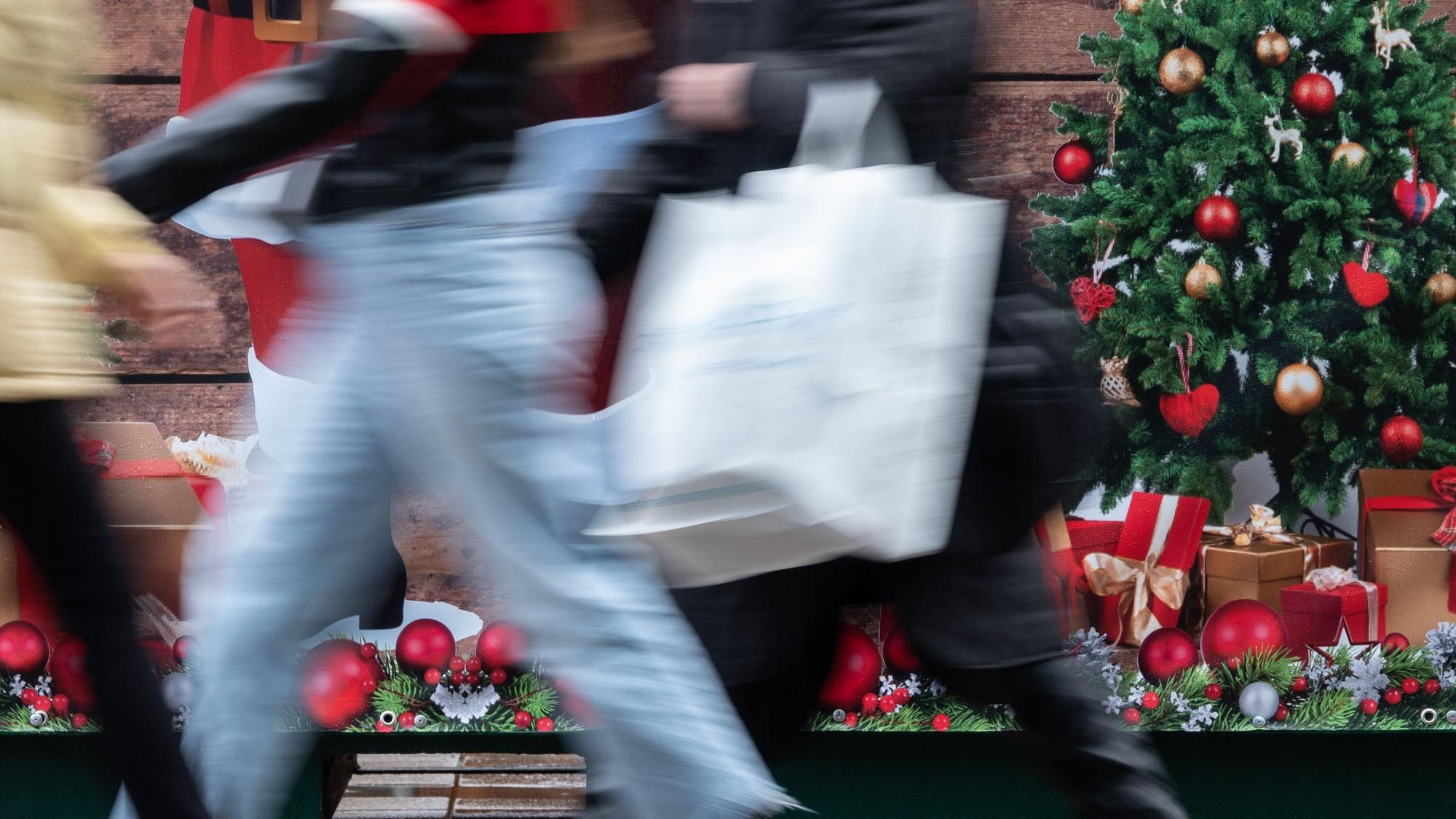 Passanten gehen an einem weihnachtlich geschmückten Verkaufsstand vorbei.