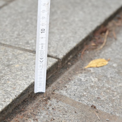 Ein Zollstock zeigt einen Höhenunterschied von zwei Zentimetern zwischen Regenrinne und Bodenbelag.