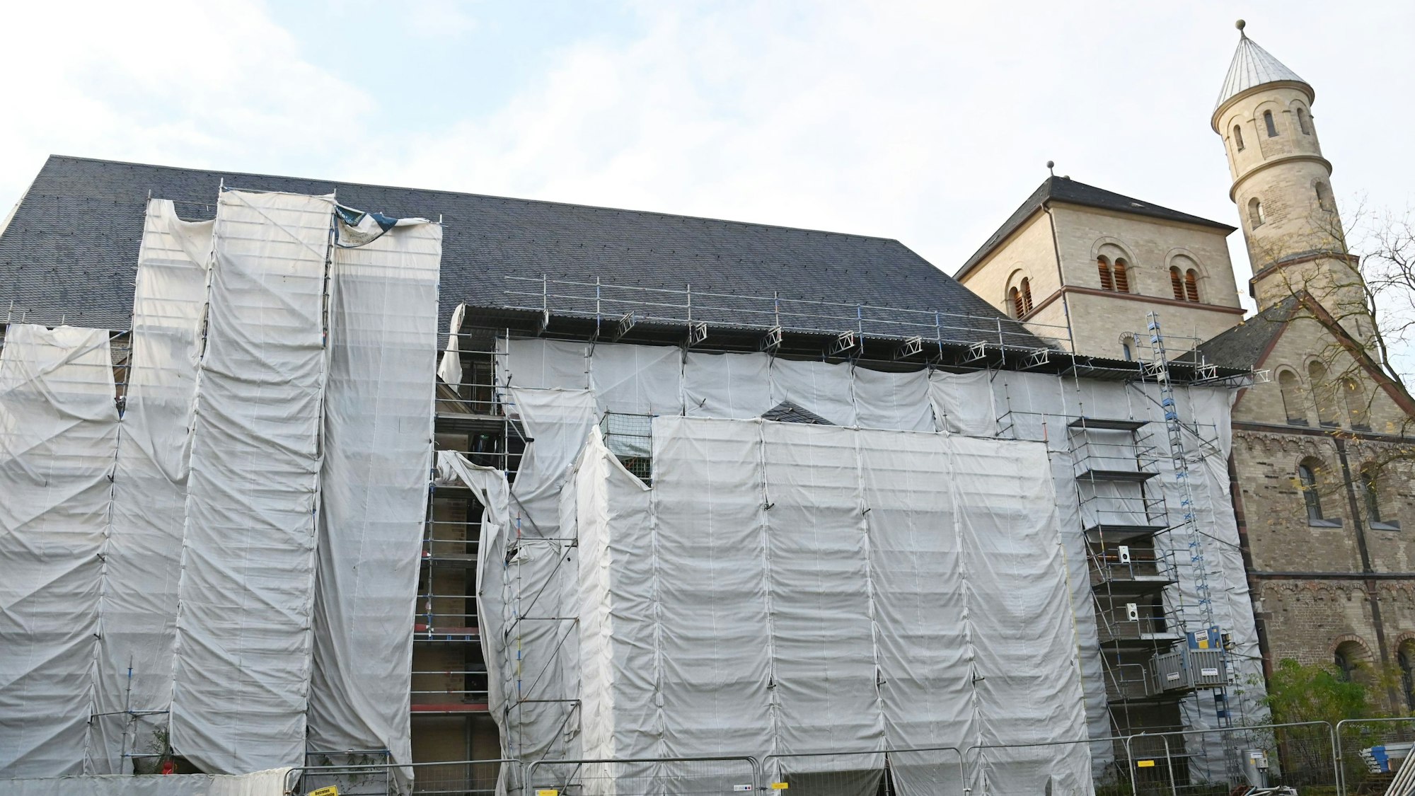 Zu sehen ist die Kirche St. Pantaleon von außen. An der Seite der Kirche sind viele weiß verhangene Baugerüst zu sehen.