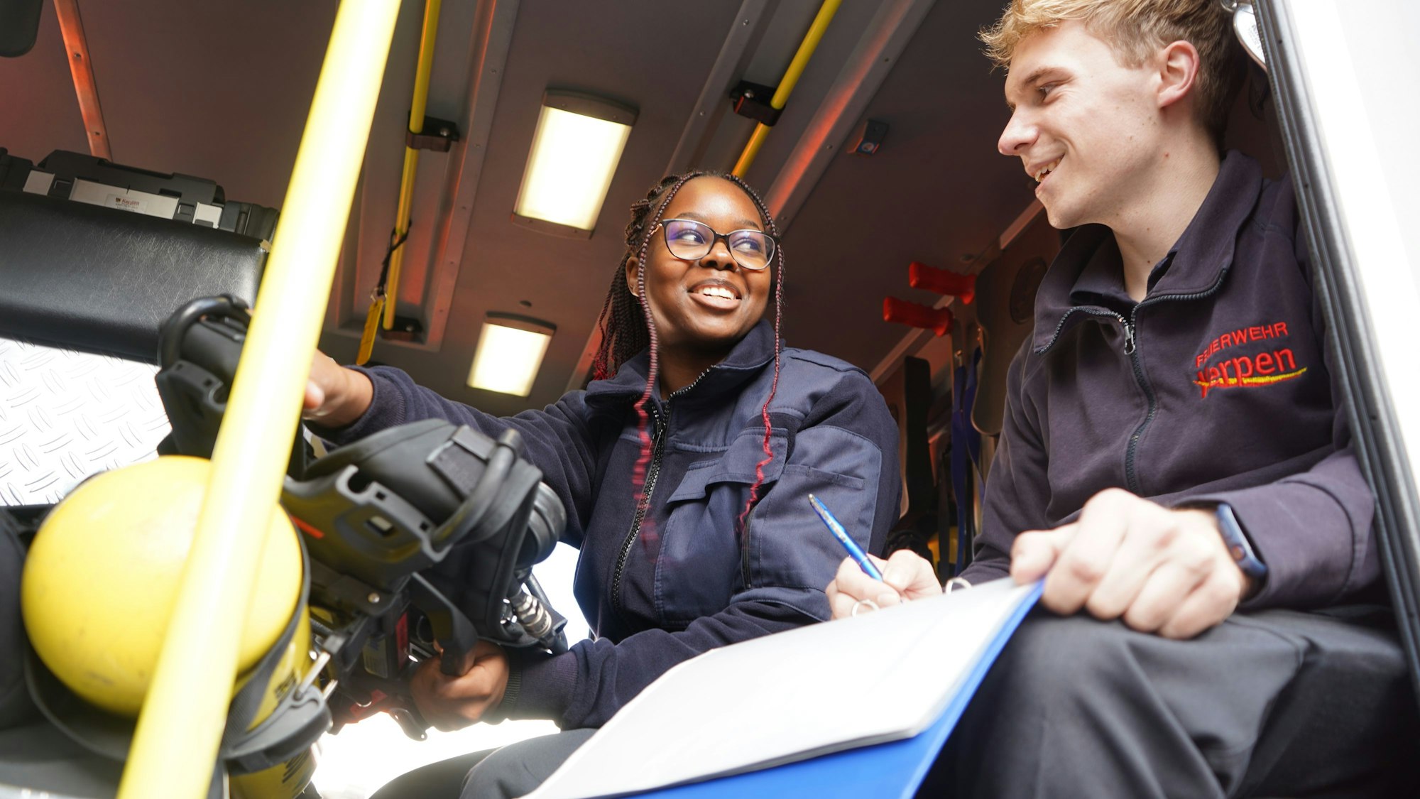 Das Foto zeigt eine junge Frau und einen jungen Mann in einem Feuerwehr-Fahrzeug.