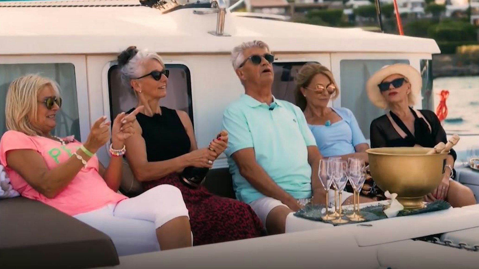 Sabine (zweite von links) öffnet eine Sektflasche auf einem Katamaran. Drei weitere Kandidatinnen und der Golden Bachelor sehen ihr dabei zu.