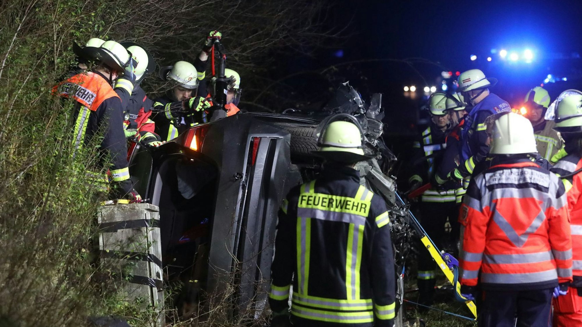 Rettungskräfte vor einem auf der Seite im Straßengraben liegenden Auto.